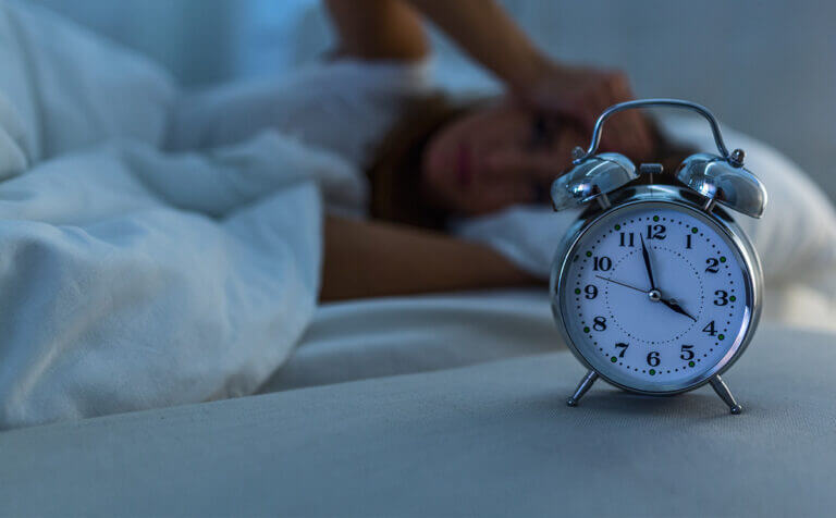 Ženska, ki ne mkore spati in budilka v ospredju.